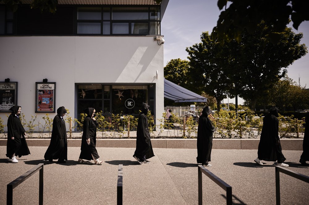 A group of people is walking around a city in a black clothing.