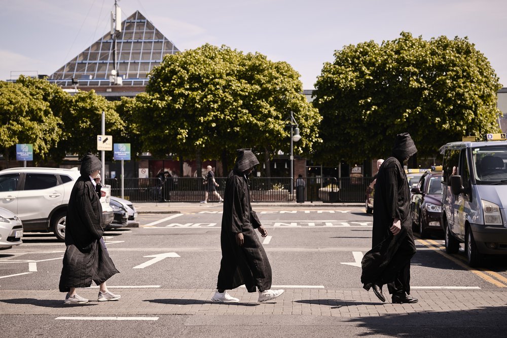 A group of people is walking around a city in a black clothing.