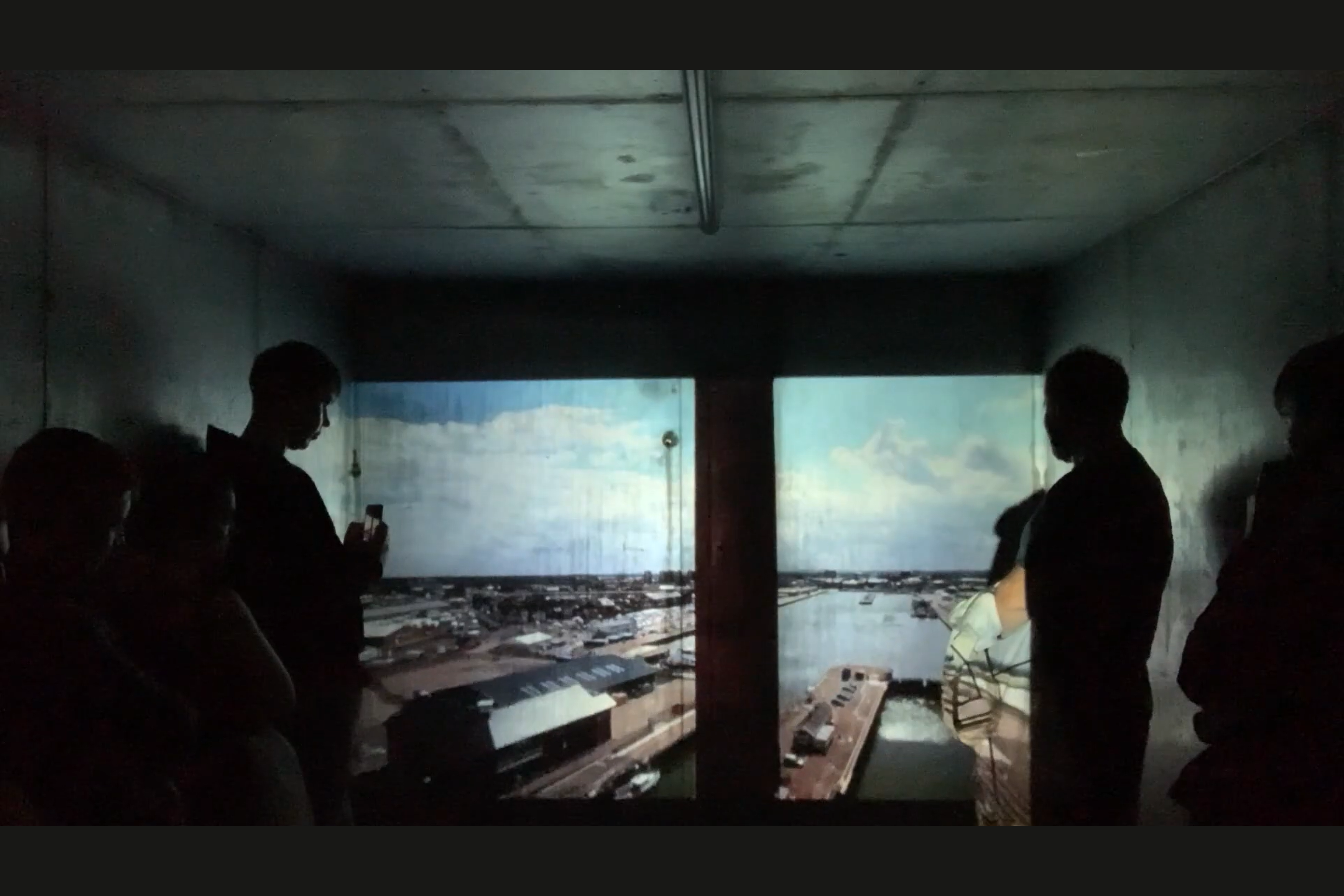 the audience are in a room with a projector and are looking at a video explaining the history of the port. 