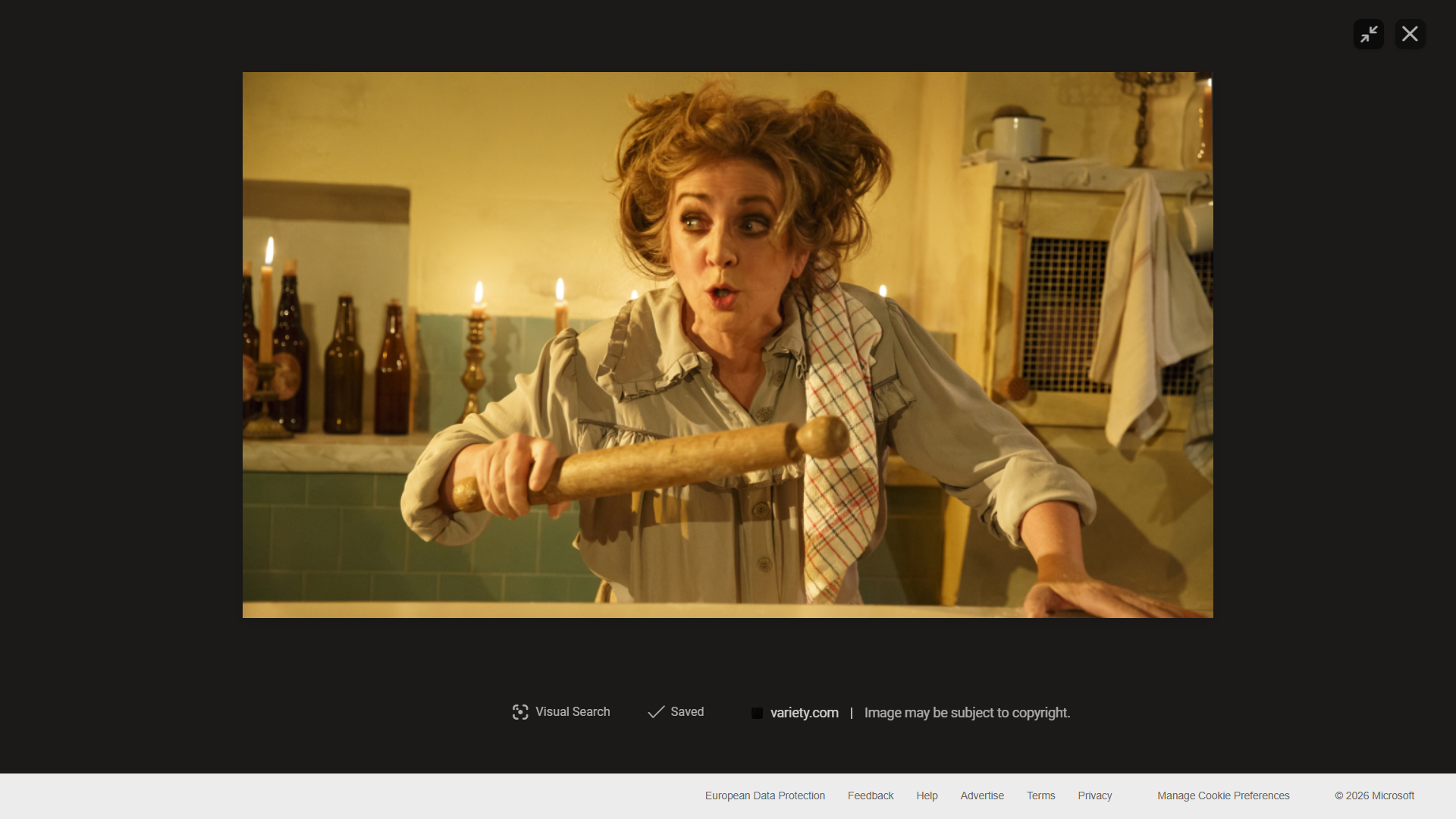 Pictured above is Siobhan McCarthy as Mrs Lovett. She is in a kitchen, with candles lighting behind her and a rolling pin in her hand. Her hair is on her head in a messy fashion and her makeup is heavy and dark around her eyes.